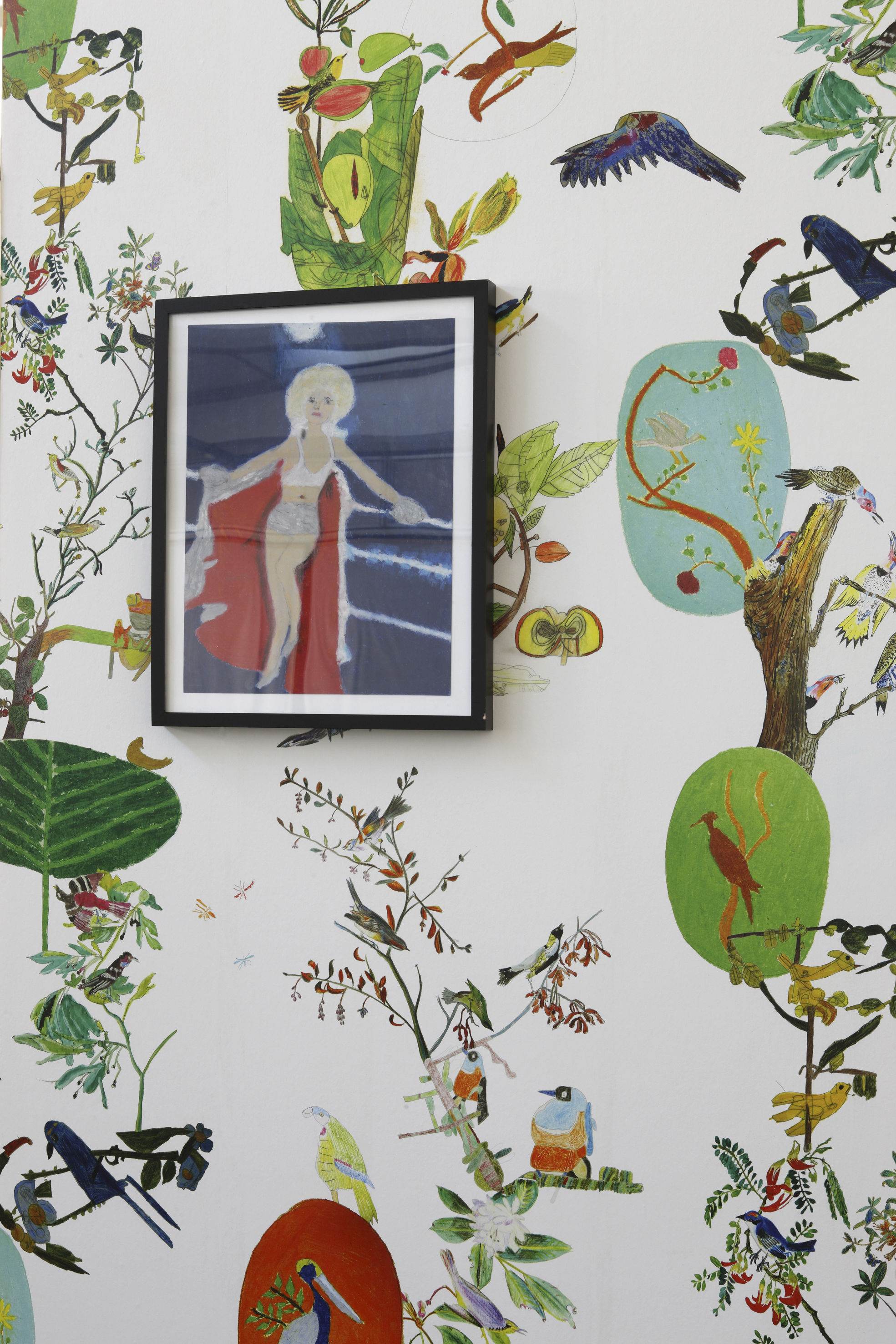 A painting of a woman with blonde hair and a cape hangs on a wallpapered wall. The wallpaper is white and decorated with colorful images of tropical birds in trees.