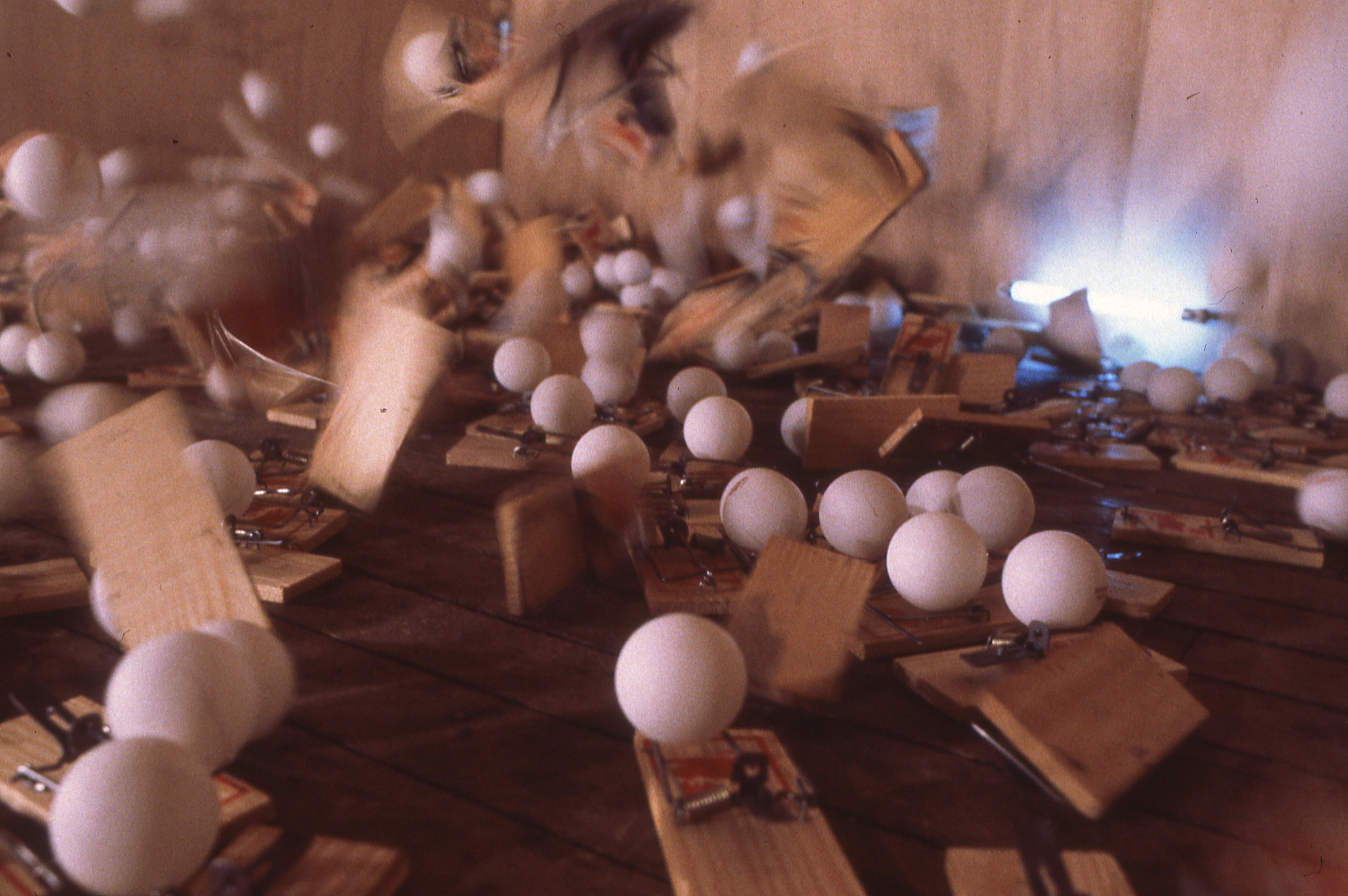 Mousetraps on a wooden floor in motion, snapping to capture ping pong balls resting atop them.
