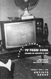 A black and white photograph of a television sitting on a low table, with a fan sitting on top of it.  White text in the bottom right reads, 