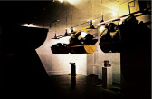 A dim photograph of hanging sculptures and multiple objects on white pedestals.