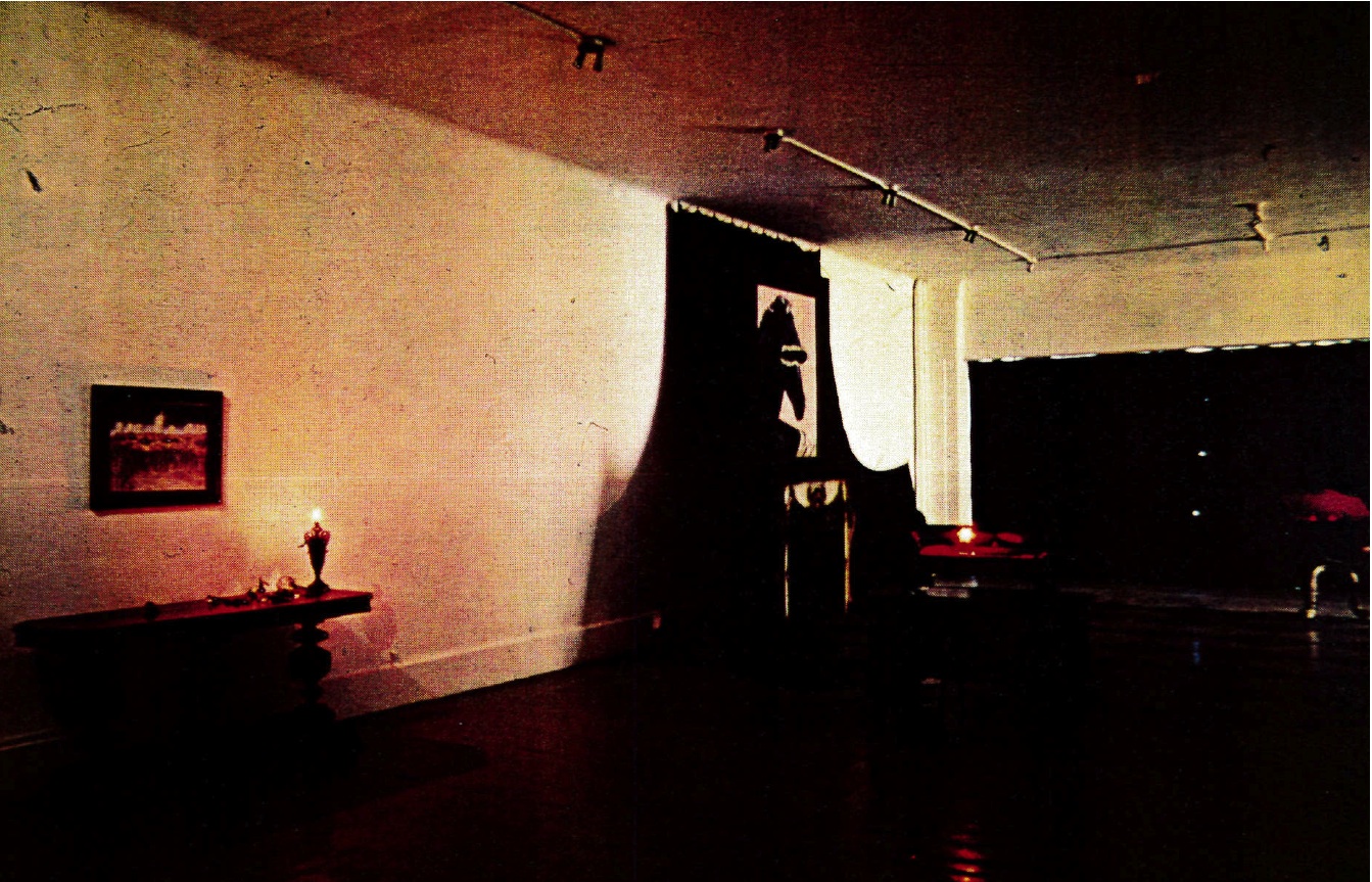 A dim photograph of dark curtains and sculptures in a gallery space.