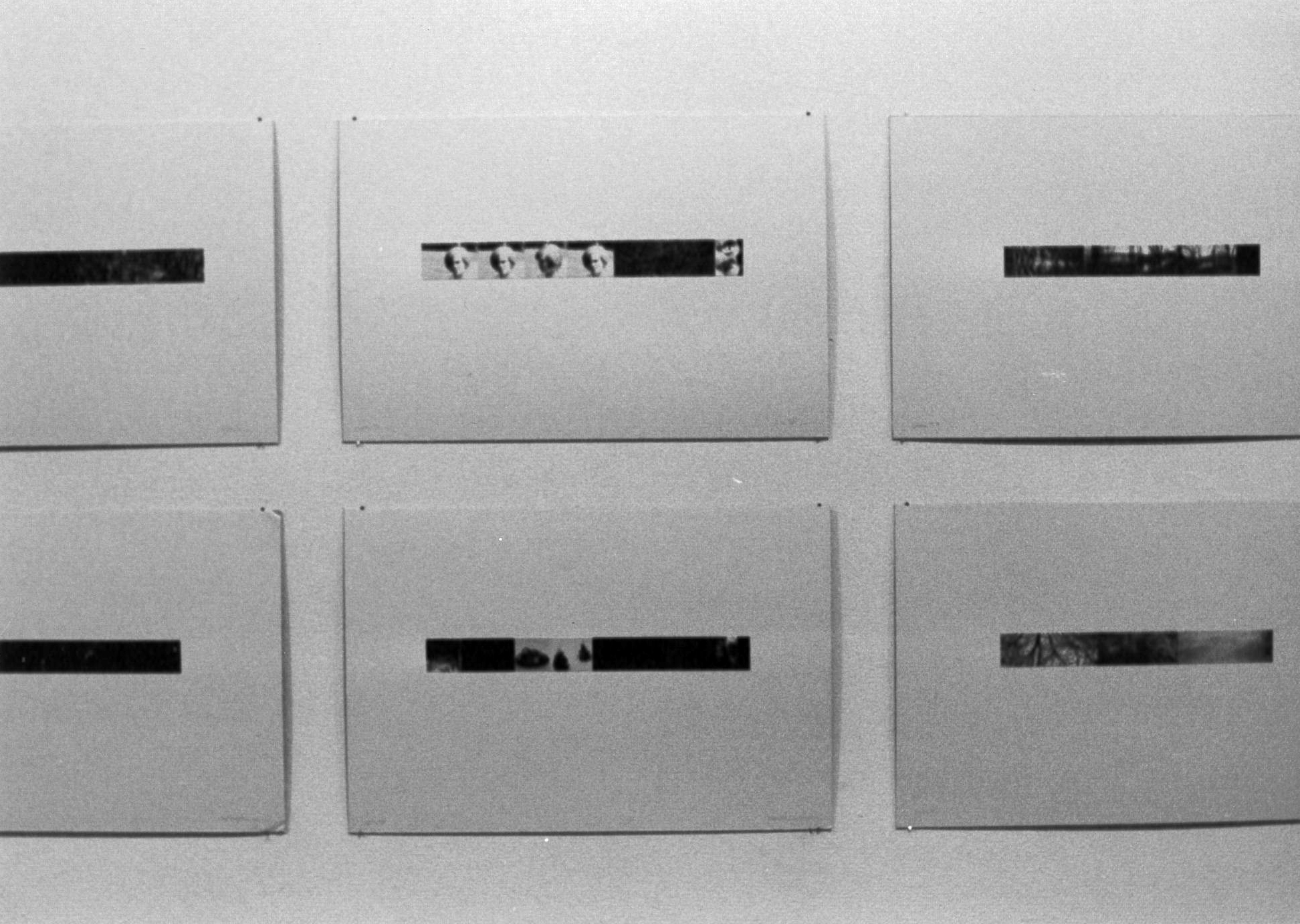 A black and white installation view of several photo strips with wide white matting attached to a wall.