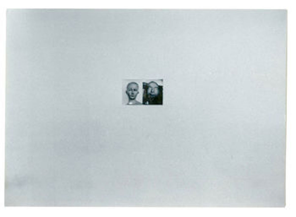 A black and white photograph of a small photograph against a white surface. The image pictured features the faces of two figures.