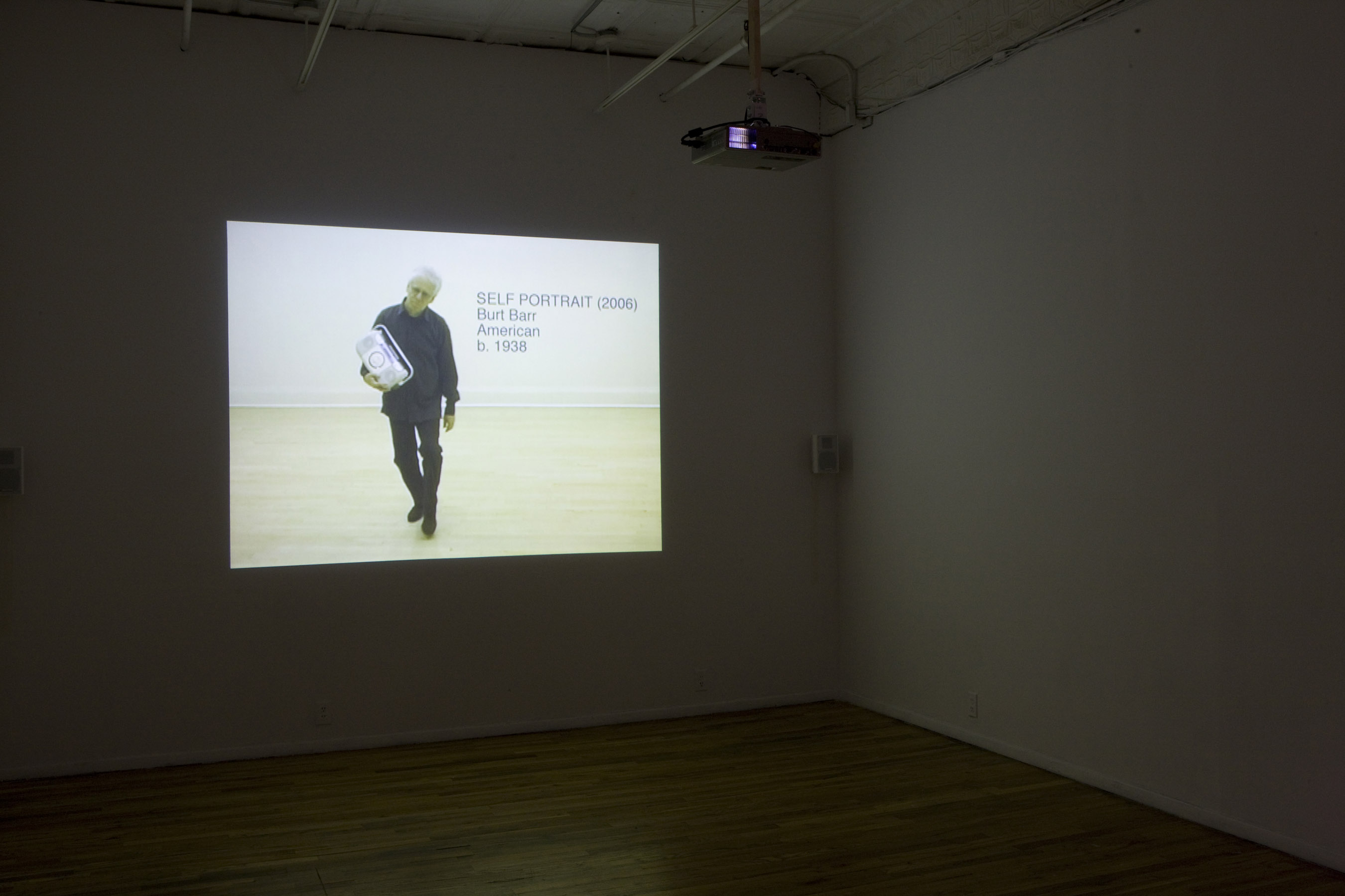 A projection on a wall in a dark room shows an image of a man holding a boombox with the text, 