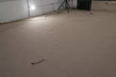 A black cord sticks out from underneath a tan carpet. Wires are visible running underneath the carpeted floor throughout the frame.