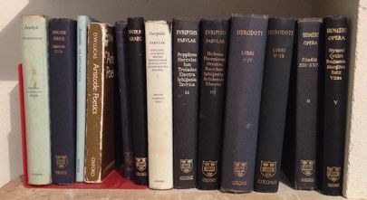 Several neutral, blue toned books, propped up by a red book stand, fill the frame on the shelf they sit in.