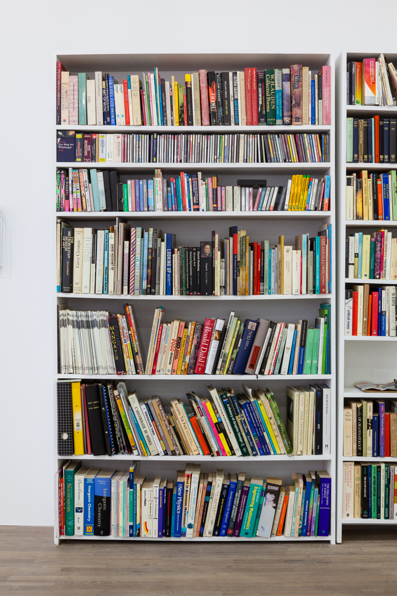 A seven shelf, white, book case is housed full of various colorful and sized books.