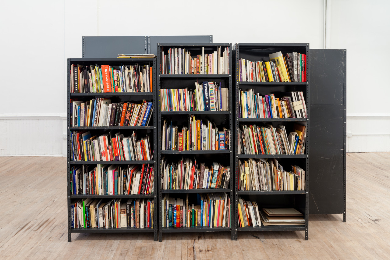 A cluster of metal book shelves sit in the middle of the room. Visible are the cubbies of three structures, populated with books of various sizes and colors.