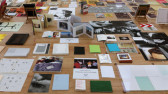 Angled view of wooden table top covered with an organized assortment of cards, books, and paper materials, displaying images and texts, in various positions.