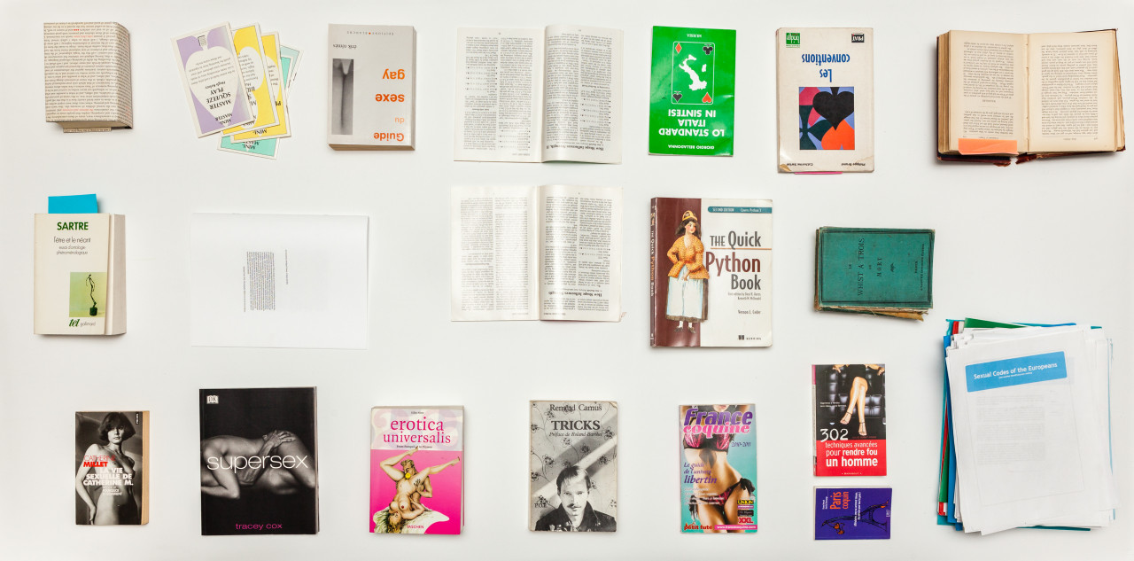 Nineteen books and documents, organized into a grid, sit against a white background. Two materials in the top center, and one on the top right, are opened to middle pages.