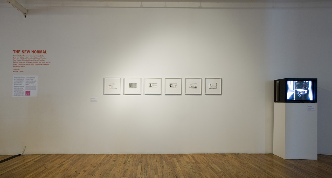 A gallery wall with six framed images of passport copies. On the right side of the images, a television stands on a white plinth, showing a black and white image. On the left side, wall text lists the exhibition title and artists.