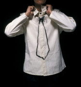 A person in a white button-down shirt with an outline of a black tie drawn on the front of the shirt. Their hands are adjusting the collar of the shirt.