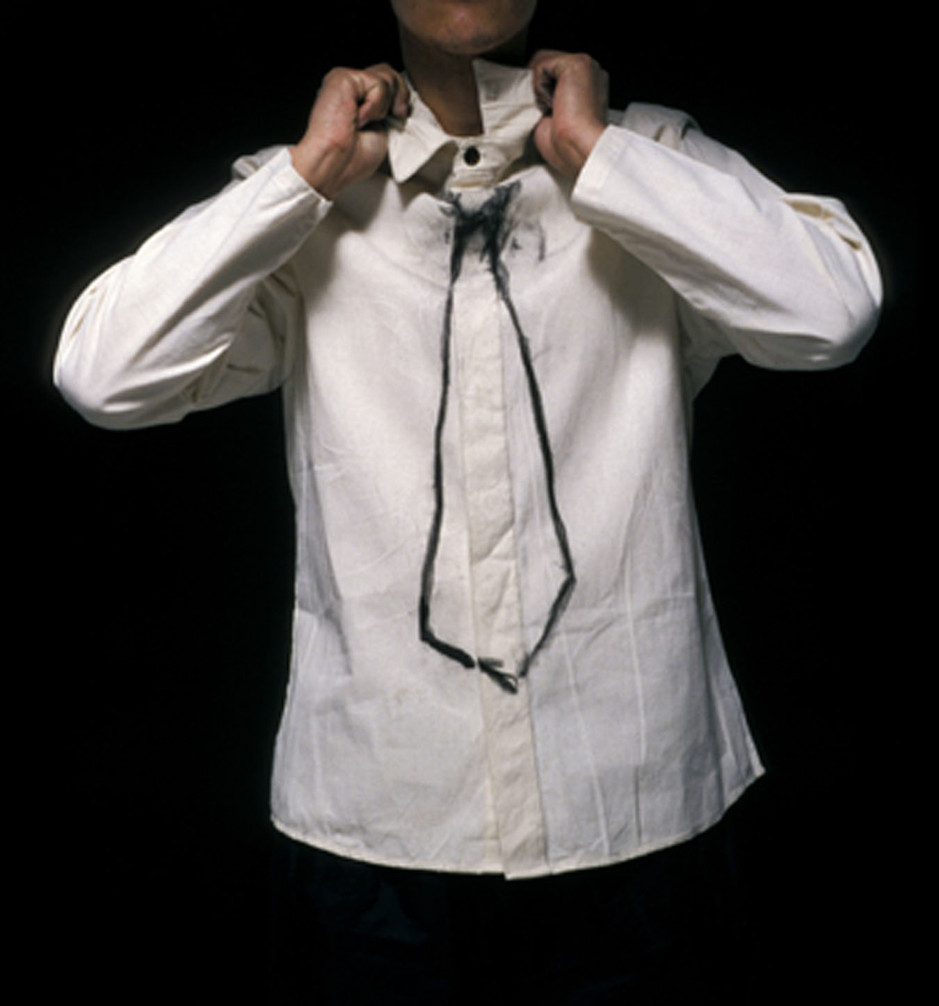 A person in a white button-down shirt with an outline of a black tie drawn on the front of the shirt. Their hands are adjusting the collar of the shirt.