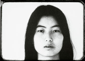Black-and-white still of a woman's face, shown from the neck up, looking forward.