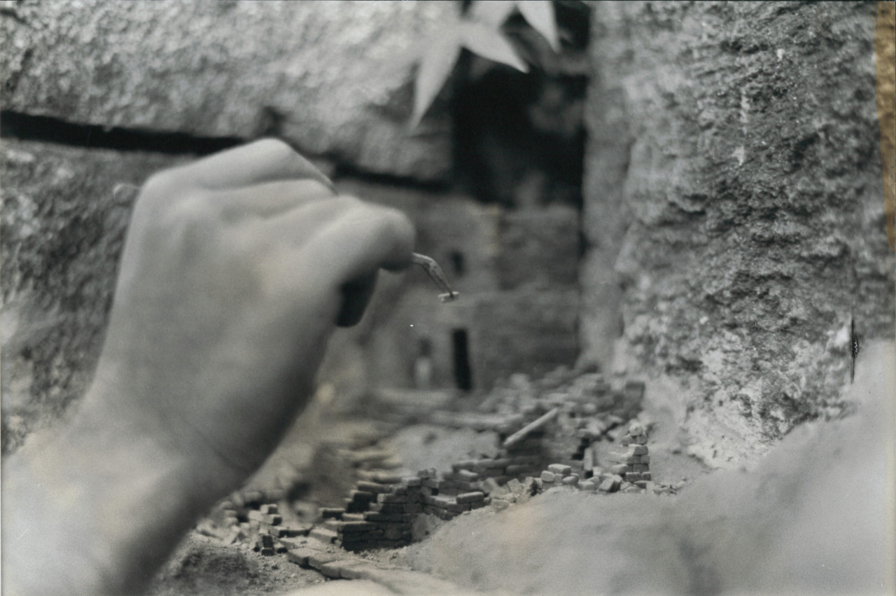 A black and white still of a hand delicately reaching out to touch a stone surface.