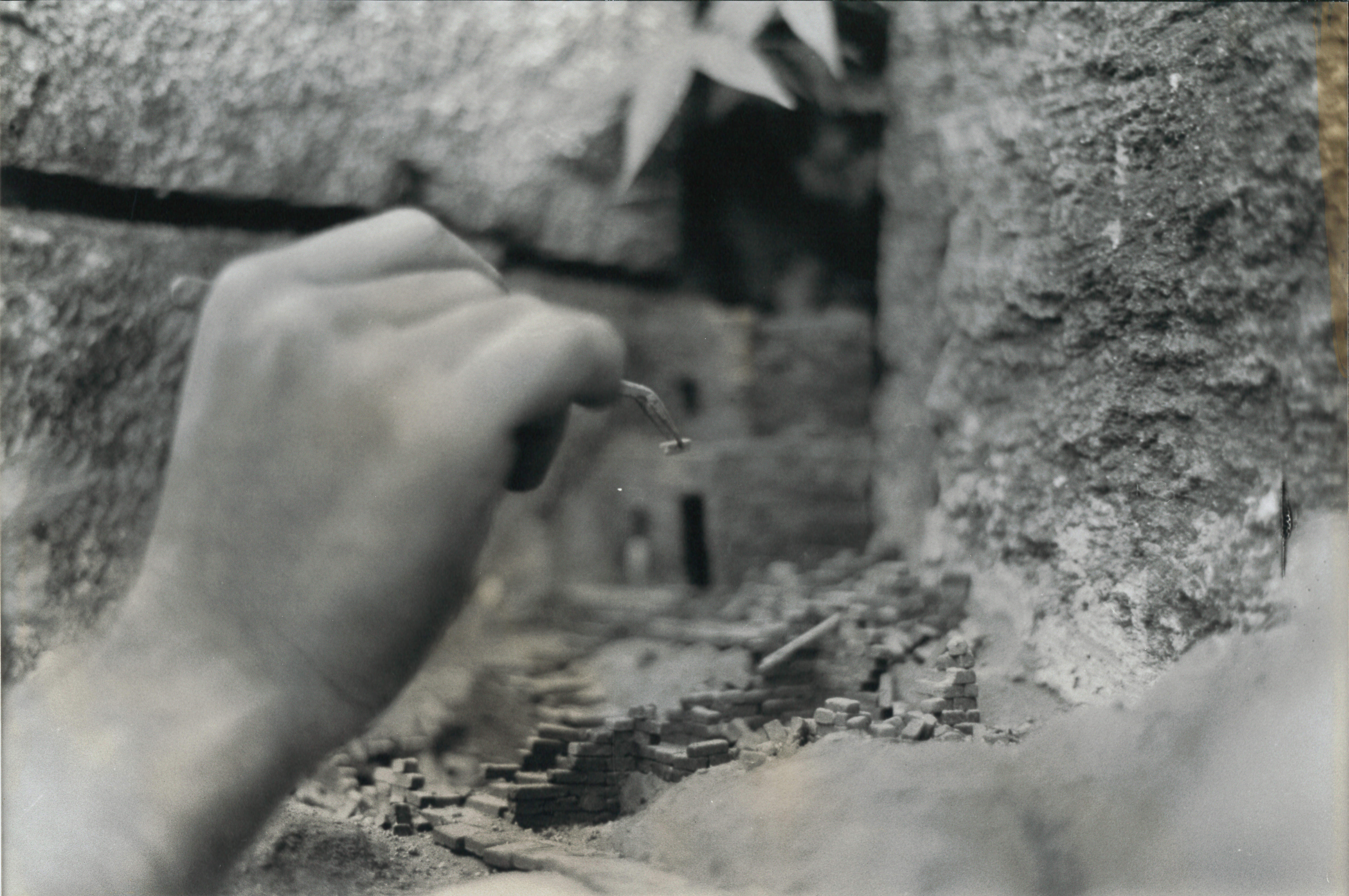 A black and white still of a hand delicately reaching out to touch a stone surface.