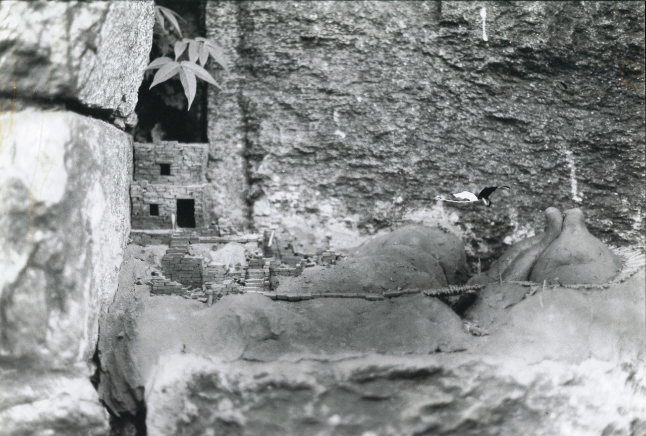 A black and white film still of a stone rockface with a small stone shelter built into the rock on the left side.