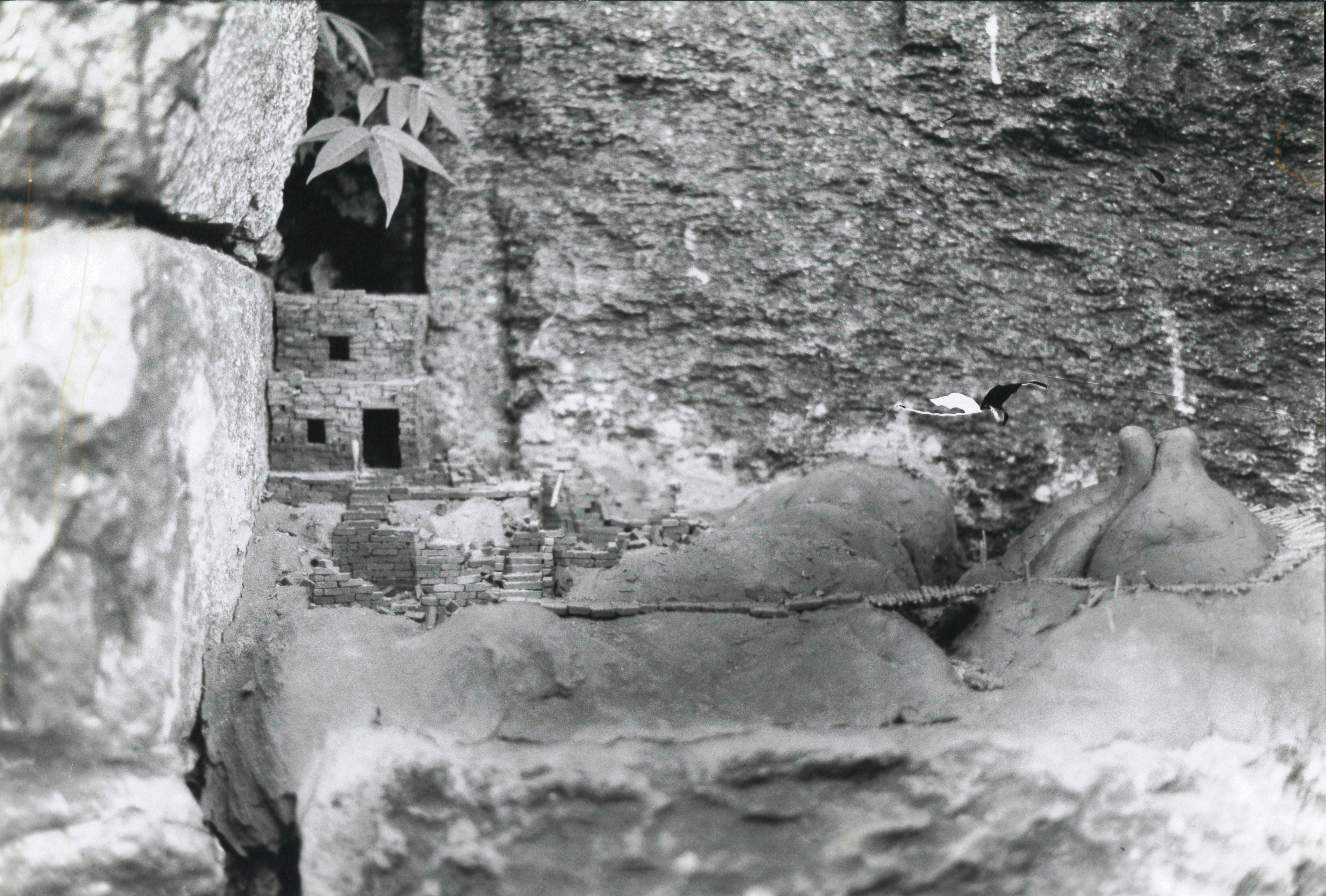 A black and white film still of a stone rockface with a small stone shelter built into the rock on the left side.