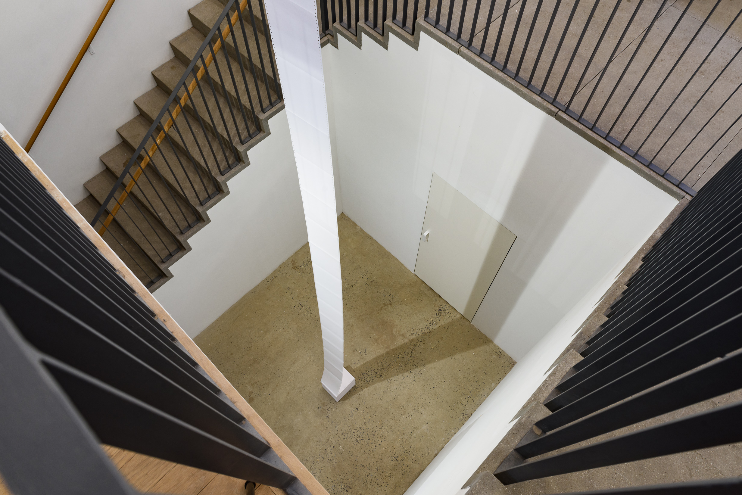 A long sheet of paper is suspended over the gallery floor. Handrails for the stairs are visible on each side of the photograph.