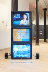 A photograph of three TV screens stacked on top of each other. Two small speakers are visible on either side of the TV screens.