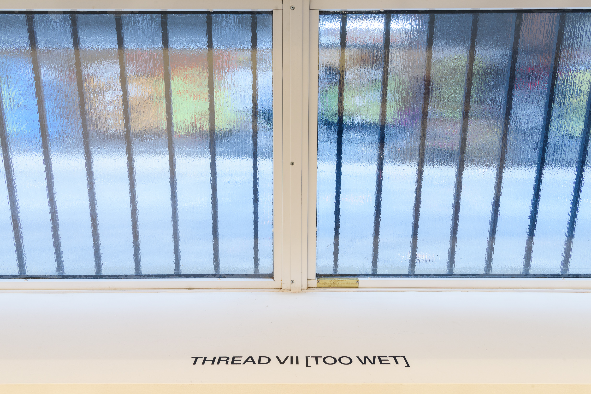 A photograph of a foggy gallery window. The words on the windowsill read 
