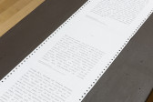 A photograph of a long sheet of dot matrix paper with text on a black table.