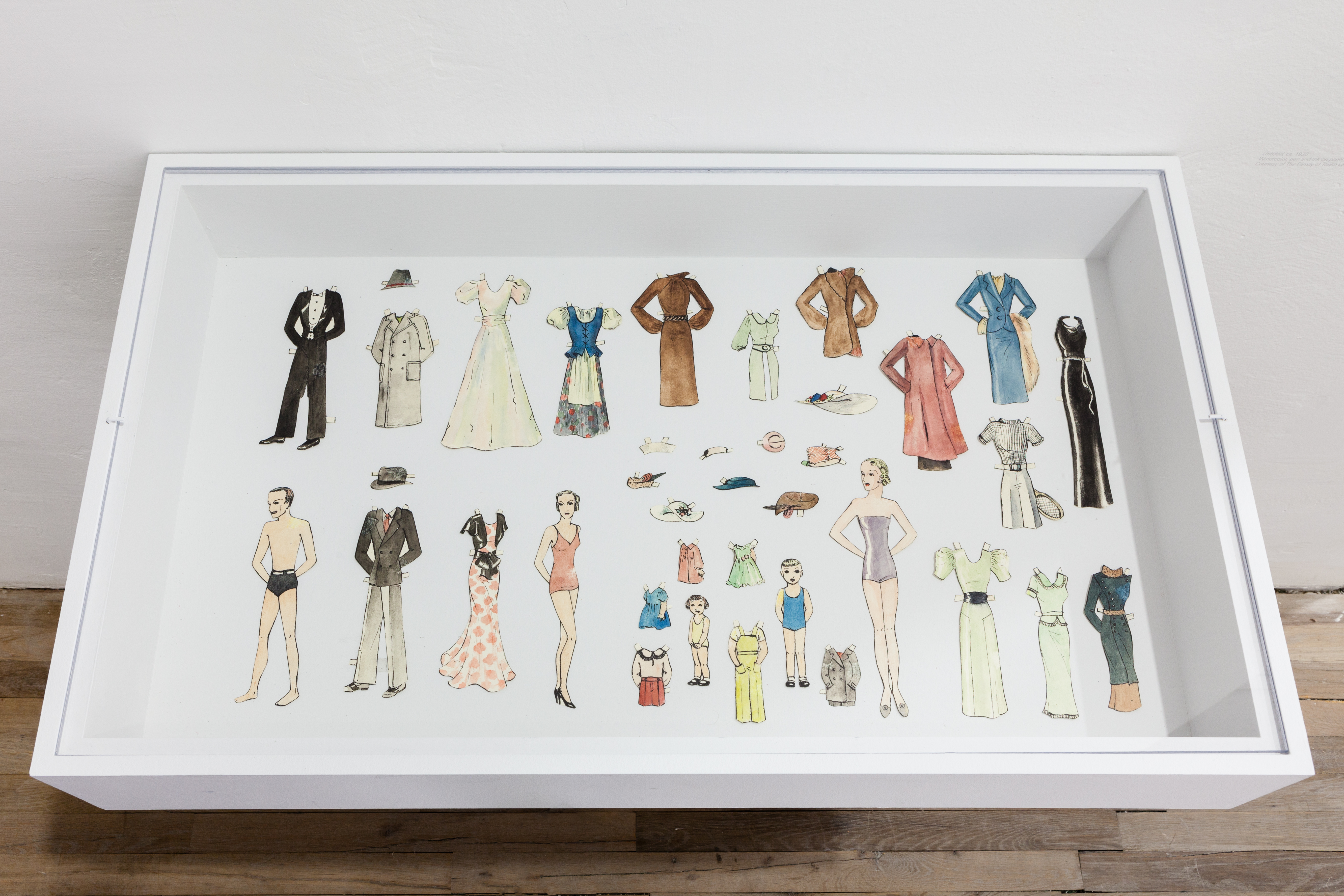 A vitrine displaying a nuclear family of paper dolls with their various options of clothing.