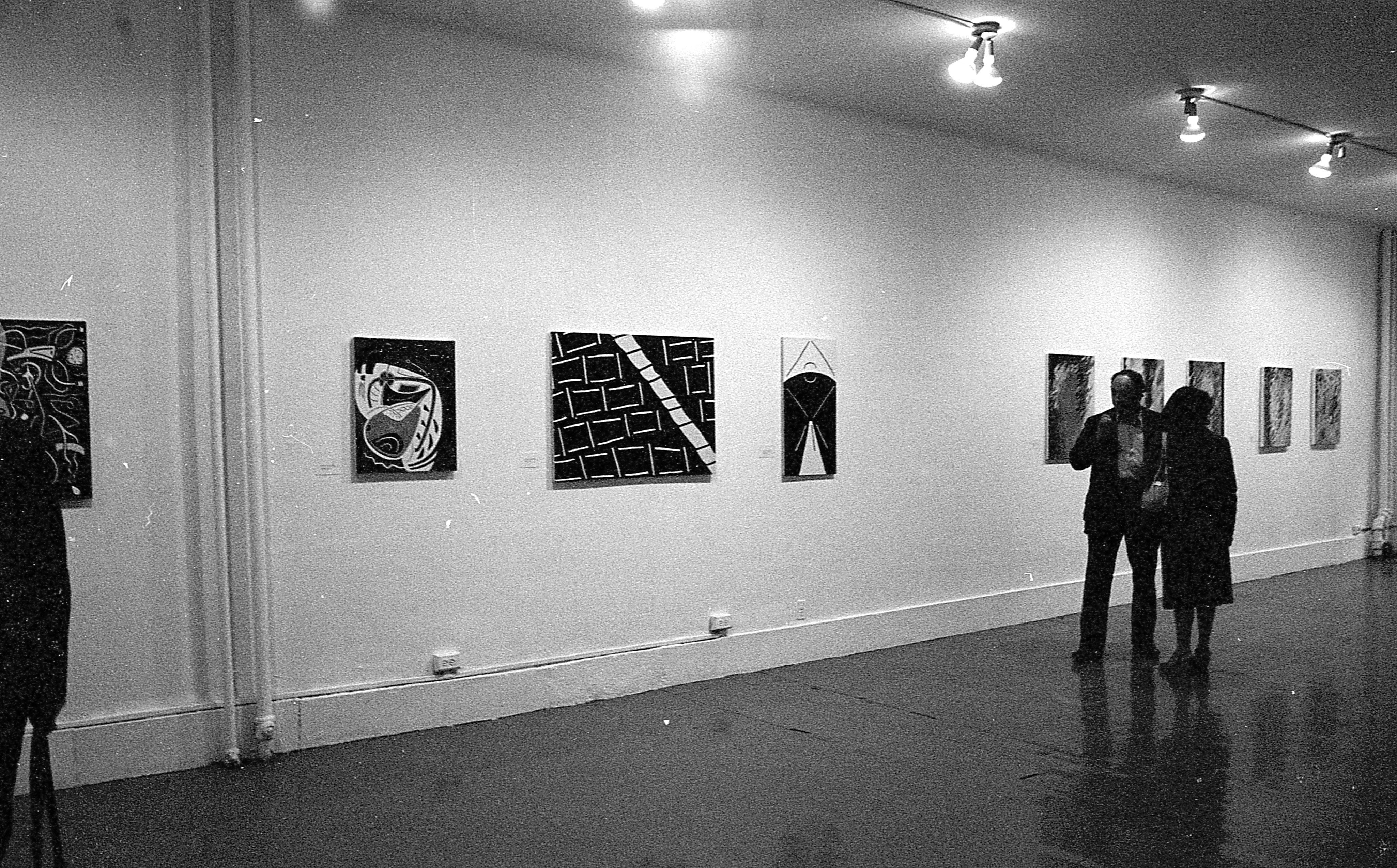 Various paintings hang on the walls as guests enjoy the exhibition opening.