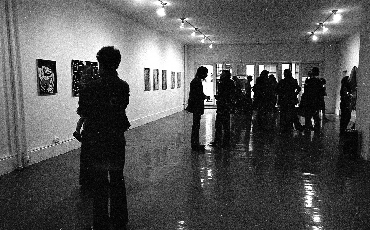 Various paintings hang on the walls as guests enjoy the exhibition opening.