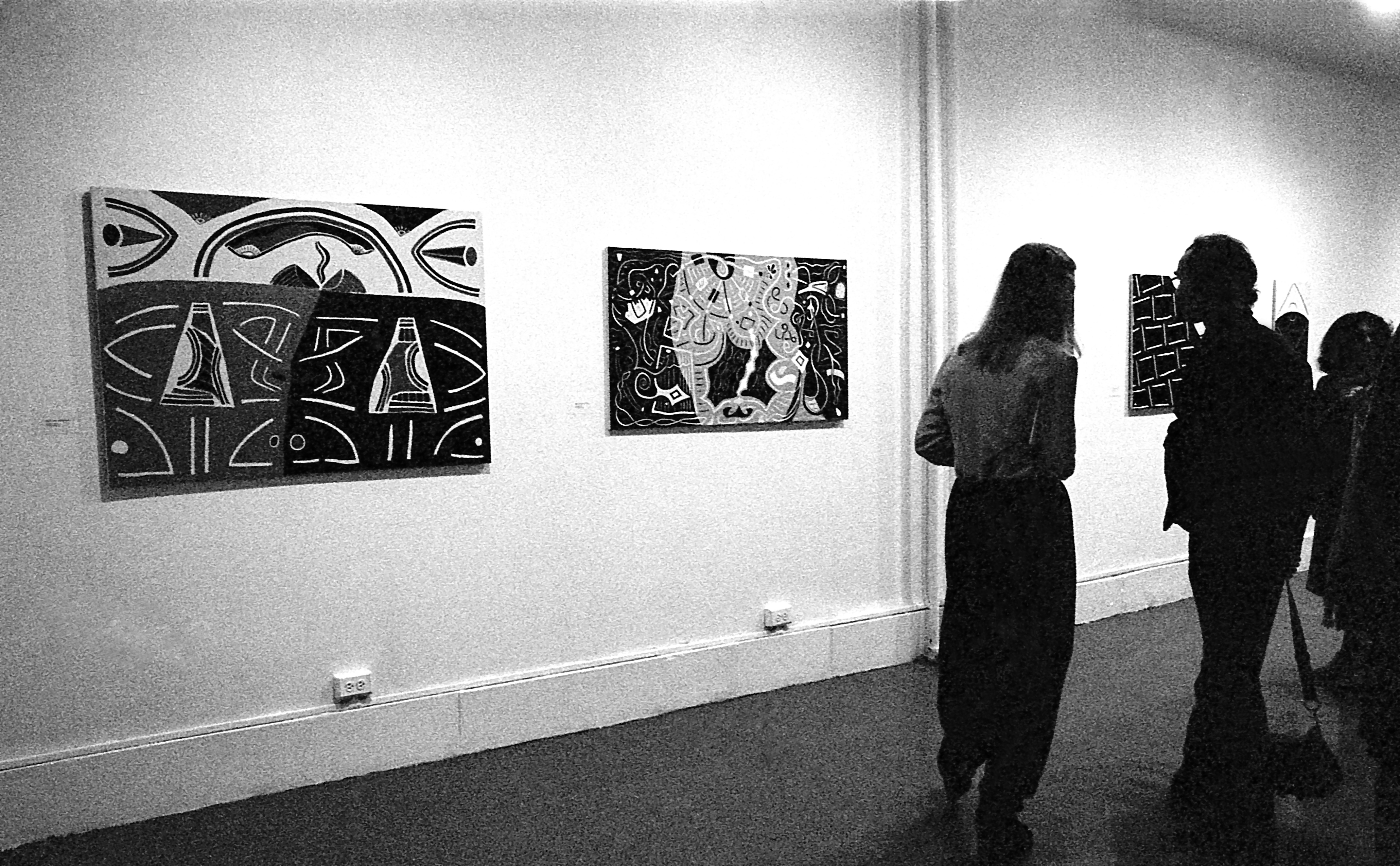 Various paintings hang on the walls as guests enjoy the exhibition opening.
