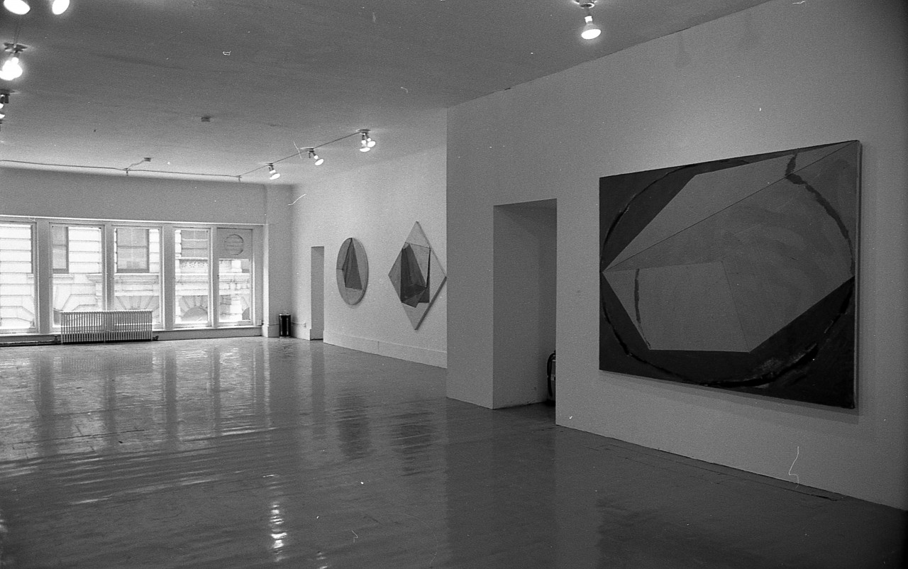 3 large paintings hang on the wall to the right. The foremost is rectangular, then further away is a rhombus shaped painting and lastly a circular piece.