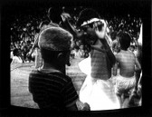 A figure stands central raising their arms while others have their back turned towards the viewer as they face an audience seated in the background. Scan lines and the surrounding box of the CRT monitor are visible in the image.