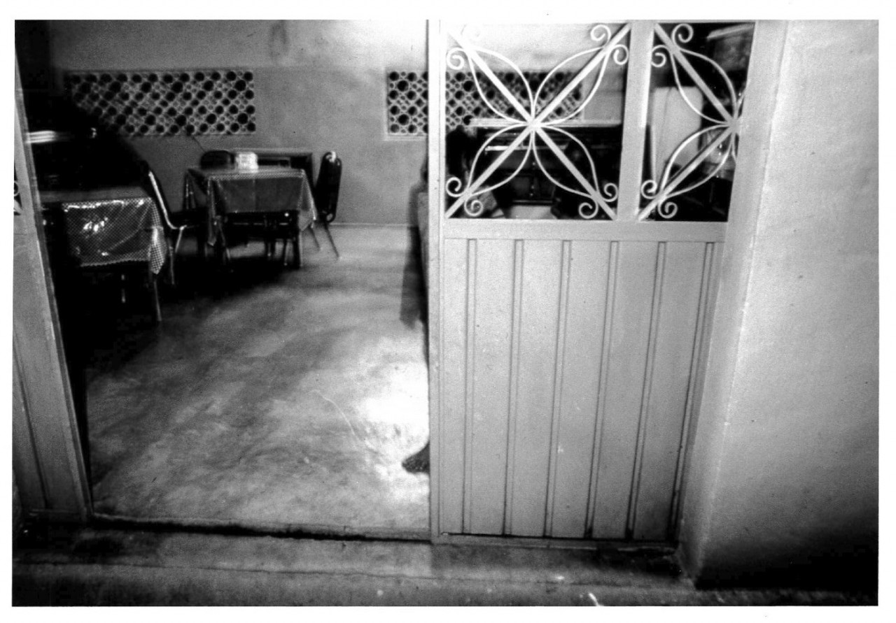 An opened gate is visible on the right with tables and chairs set up on a cement floor and decorative steel windows visible at the top.