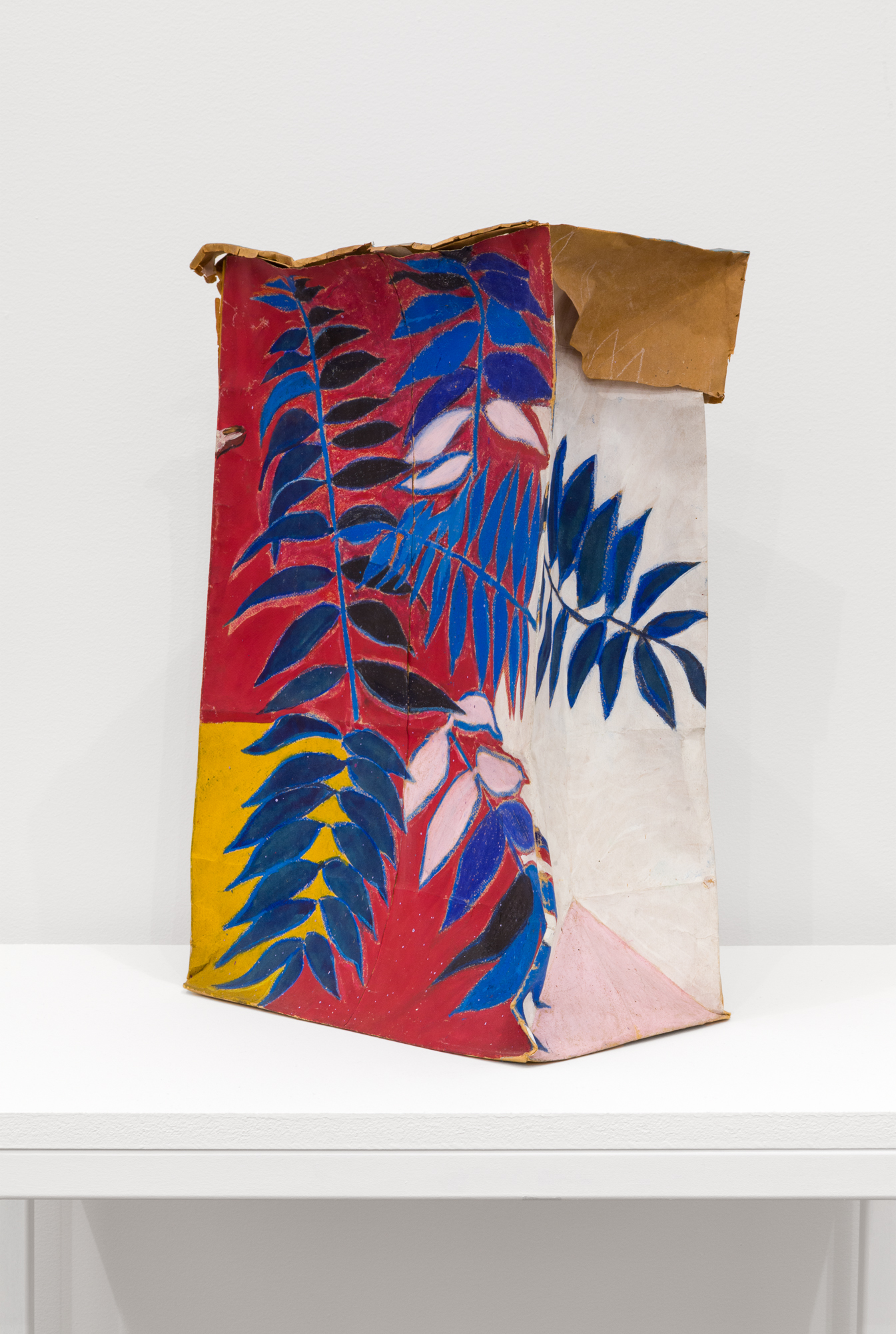 A decorated paper bag on a shelf. Blue ferns have been illustrated onto white, red, and pink backgrounds.
