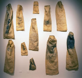 Eleven beige sacks of various sizes, depicting text and illustrations, are arranged on a wall.