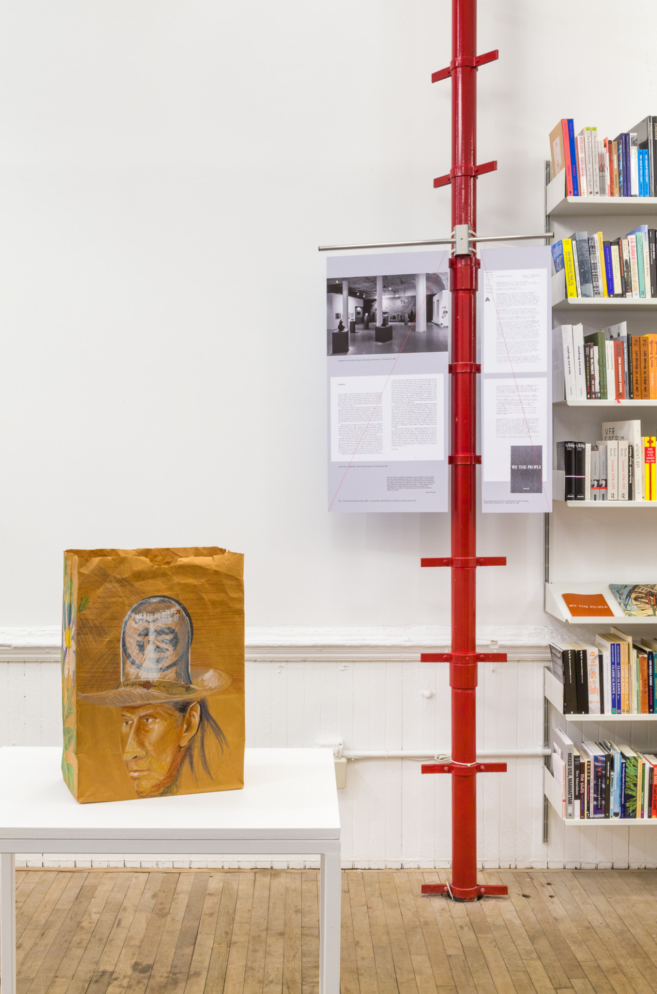 A large red pole with matching brackets stretches from floor to ceiling, holding up an spread of Artists Space