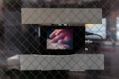 A small device with a screen and cables is stuck to a closed door with a glass window and safety guard. The screen displays a blurred close up image of two hands grazing one another.