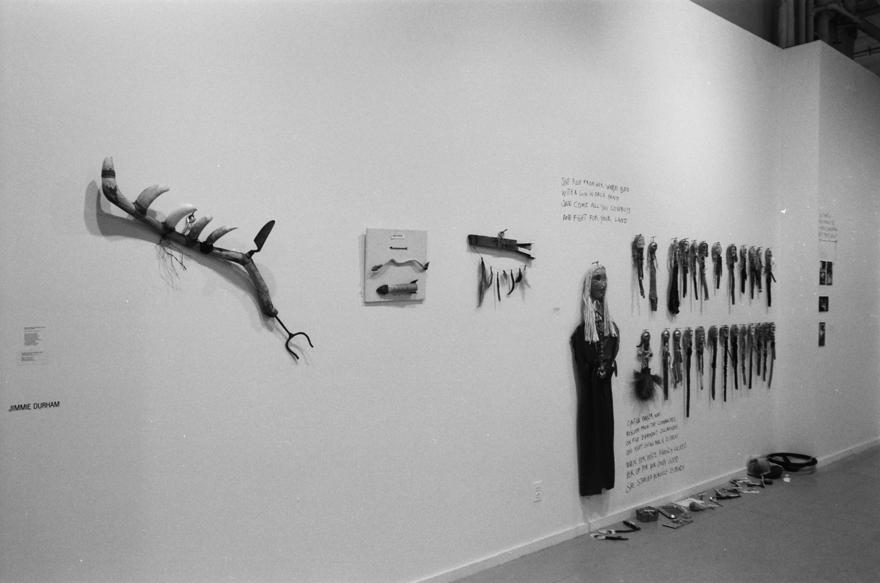 Dolls and other sculptural items appea on the wall and the floor along with text in a gallery setting.