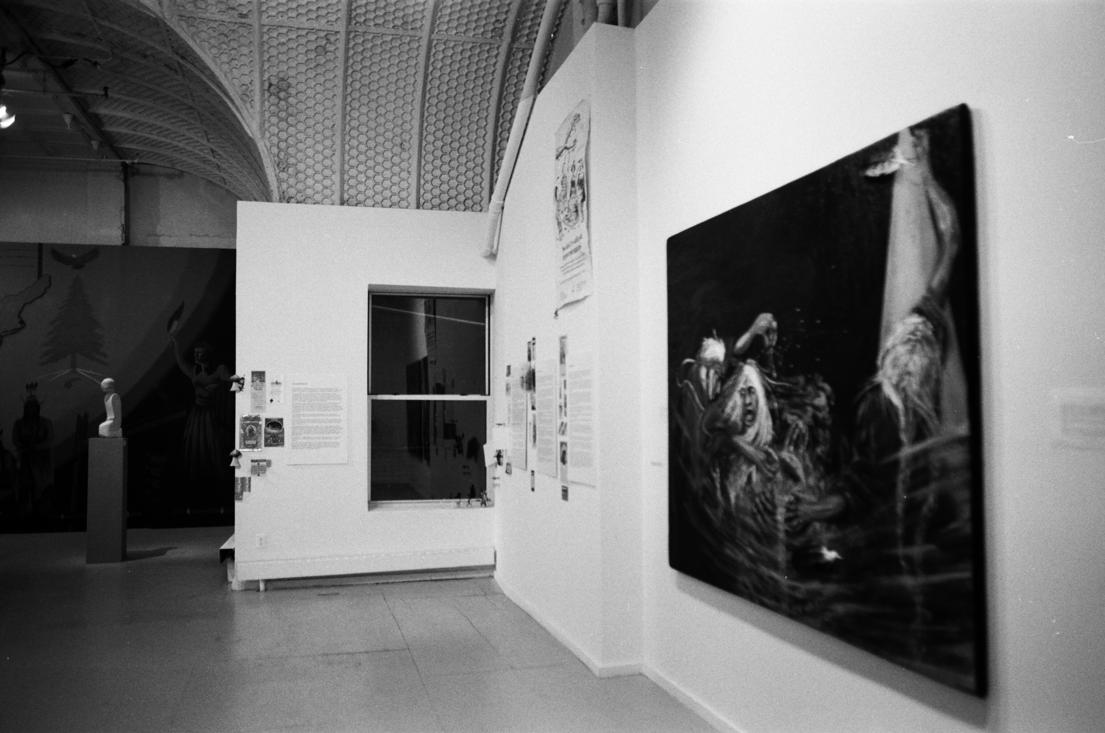 A painting can be seen on the right adjacent to walls with a number of posters on them and a window. A sculpture on a pedestal can be seen in the background. A curving ceiling is visible above.