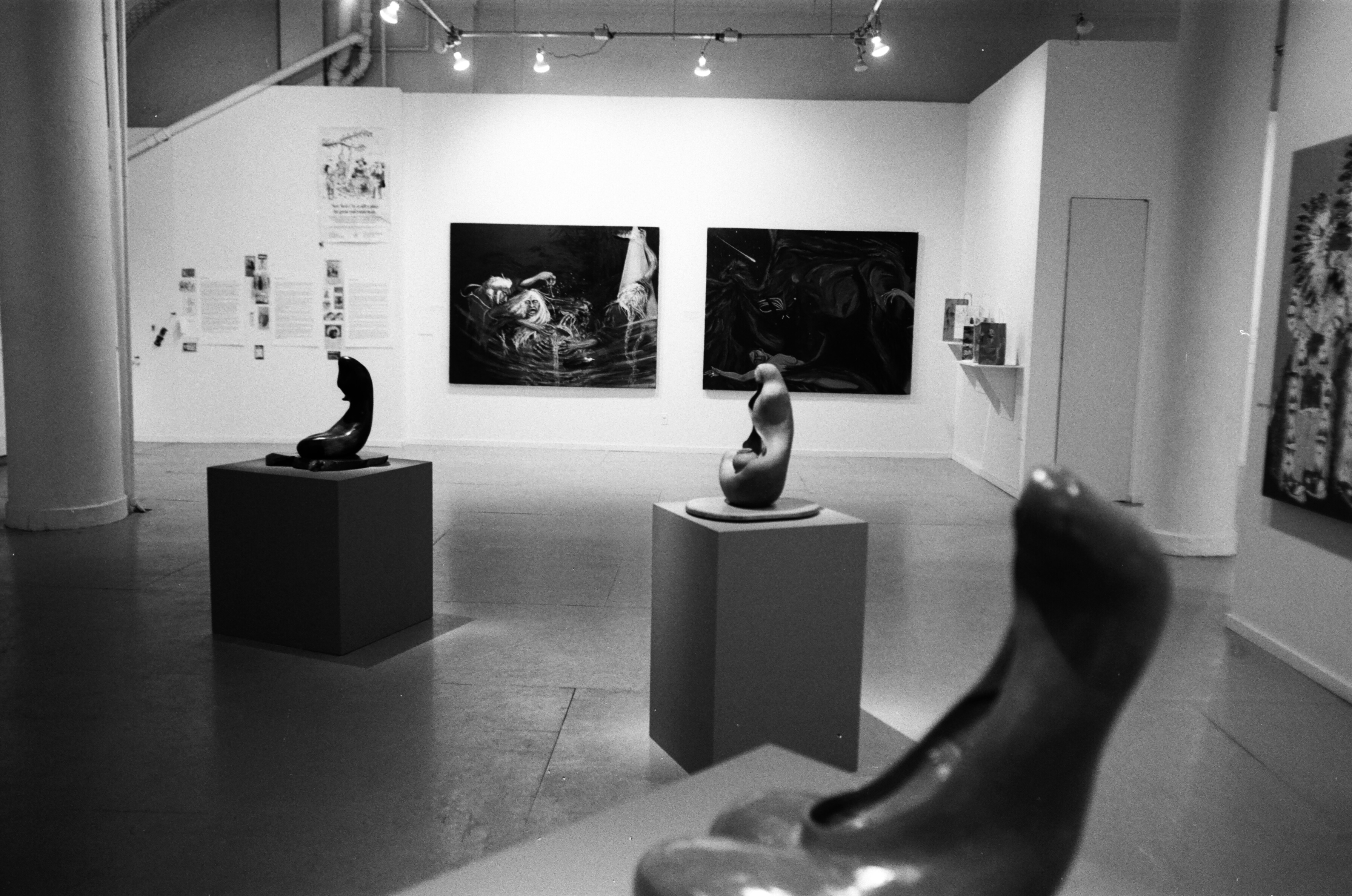 A number of sculptures on pedestals can be seen in the foreground with paintings and sculptures behind them in a gallery setting.