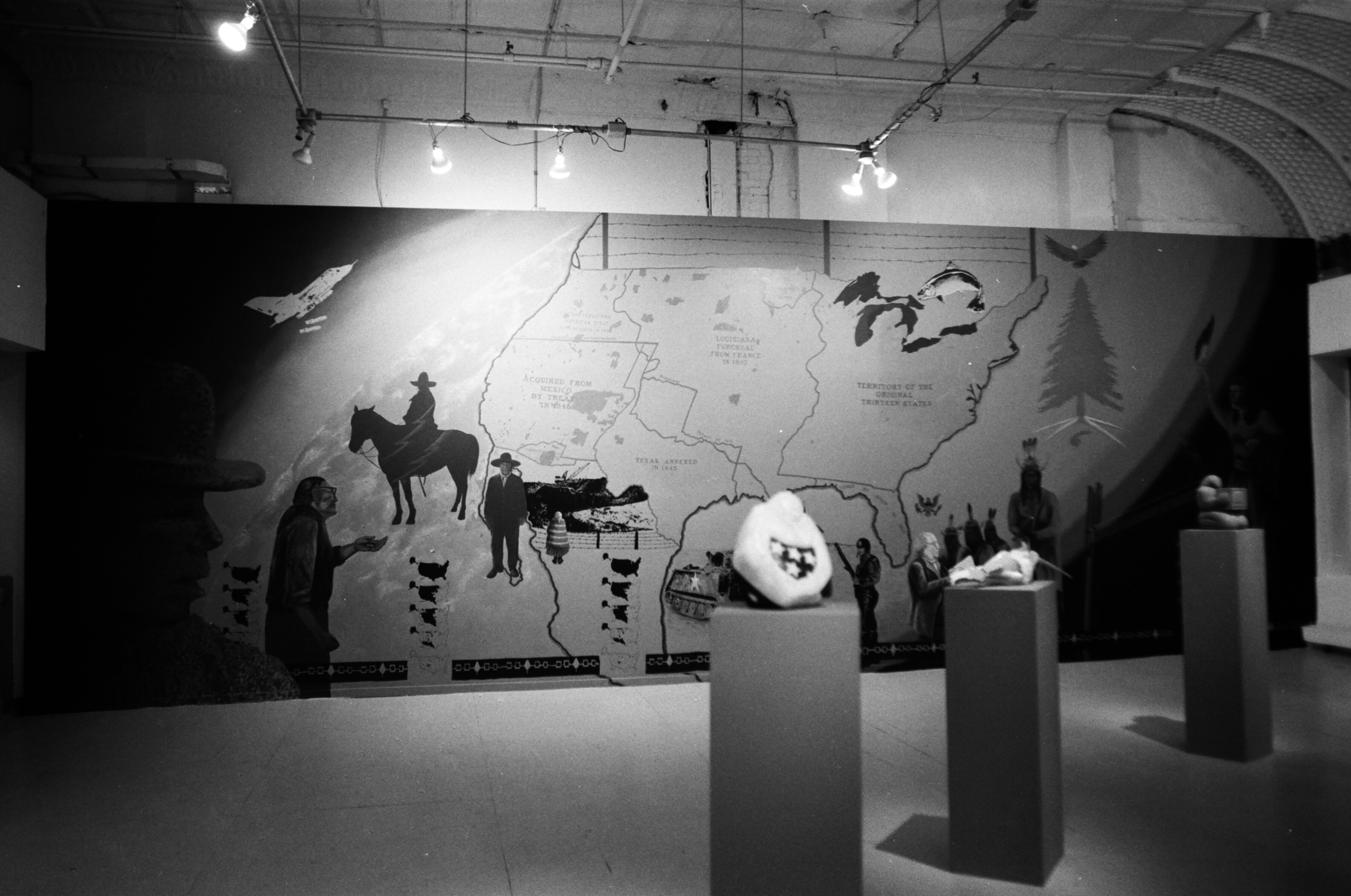 Small sculptures on pedestals are lined up diagonally in front of a map and various images.