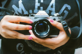 A person with pink nail polish hold up a Canon AE-1 film camera.