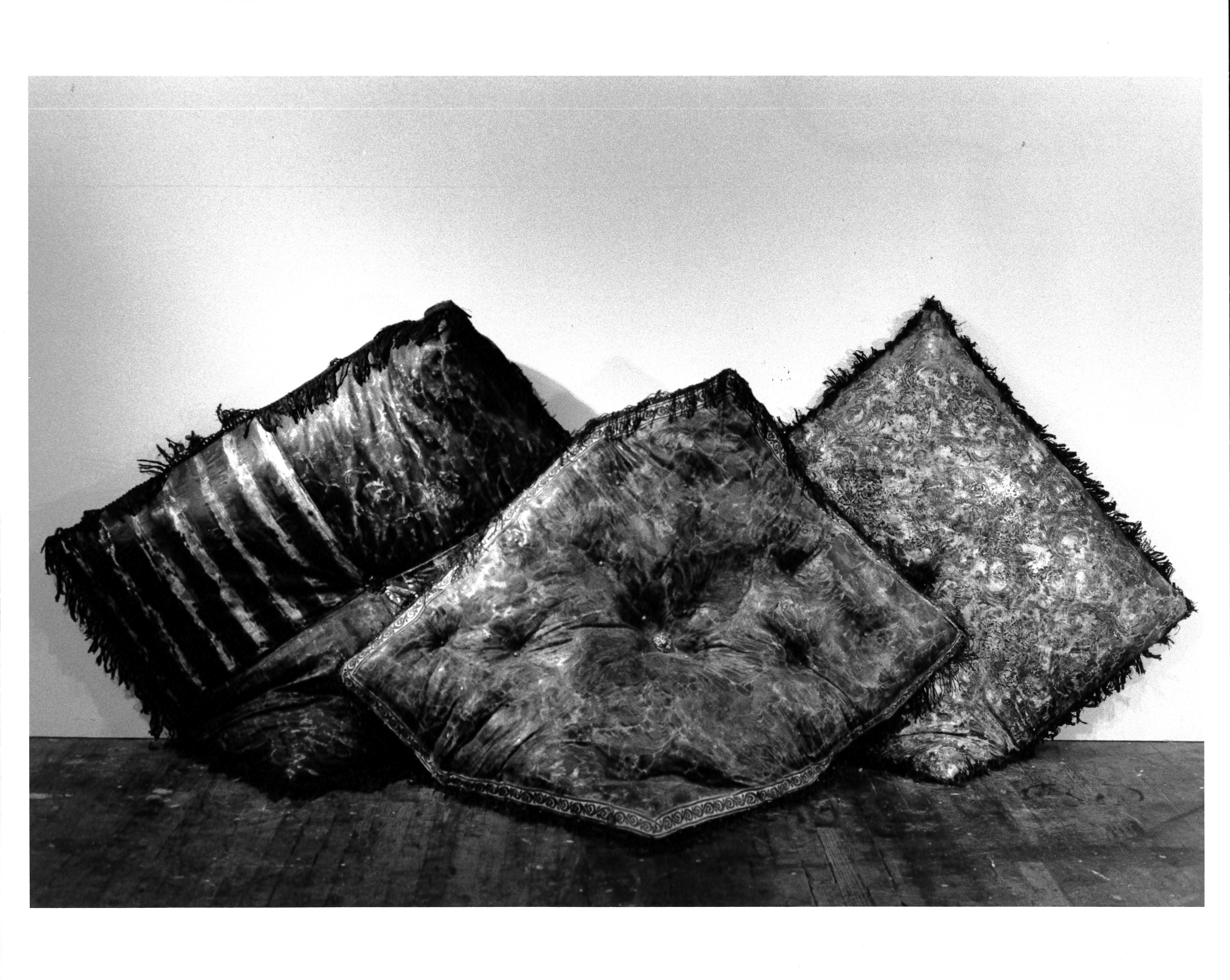 A black and white image of three overlapping pillows propped up against a white wall.