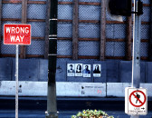 A city street with a concrete median and wall made from gray metal supported by wooden planks. The median has the words 