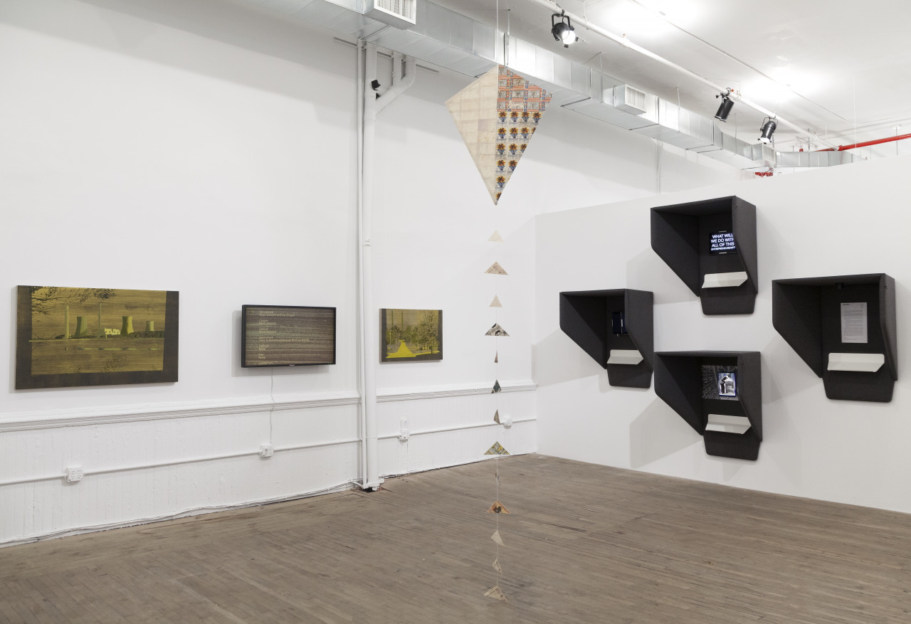 Three yellow-toned paintings hang at eye level, adjacent to four black viewing boxes installed on a gallery wall to the right of the canvases. A kite hangs from the ceiling in the middle of the exhibition space, its tail touching the floor.