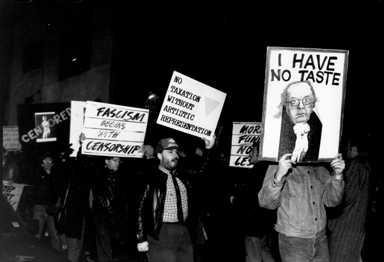 A line of people marching forward hold up signs reading, "NO TAXATION WITHOUT ARTISTIC REPRESENTATION" and "FASCISM BEGINS WITH CENSORSHIP,