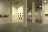 Two rooms in a large gallery space are visible, with artworks hung on the walls and sculptures in the center of the further room.