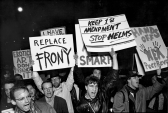 A line of people marching forward hold up signs reading 
