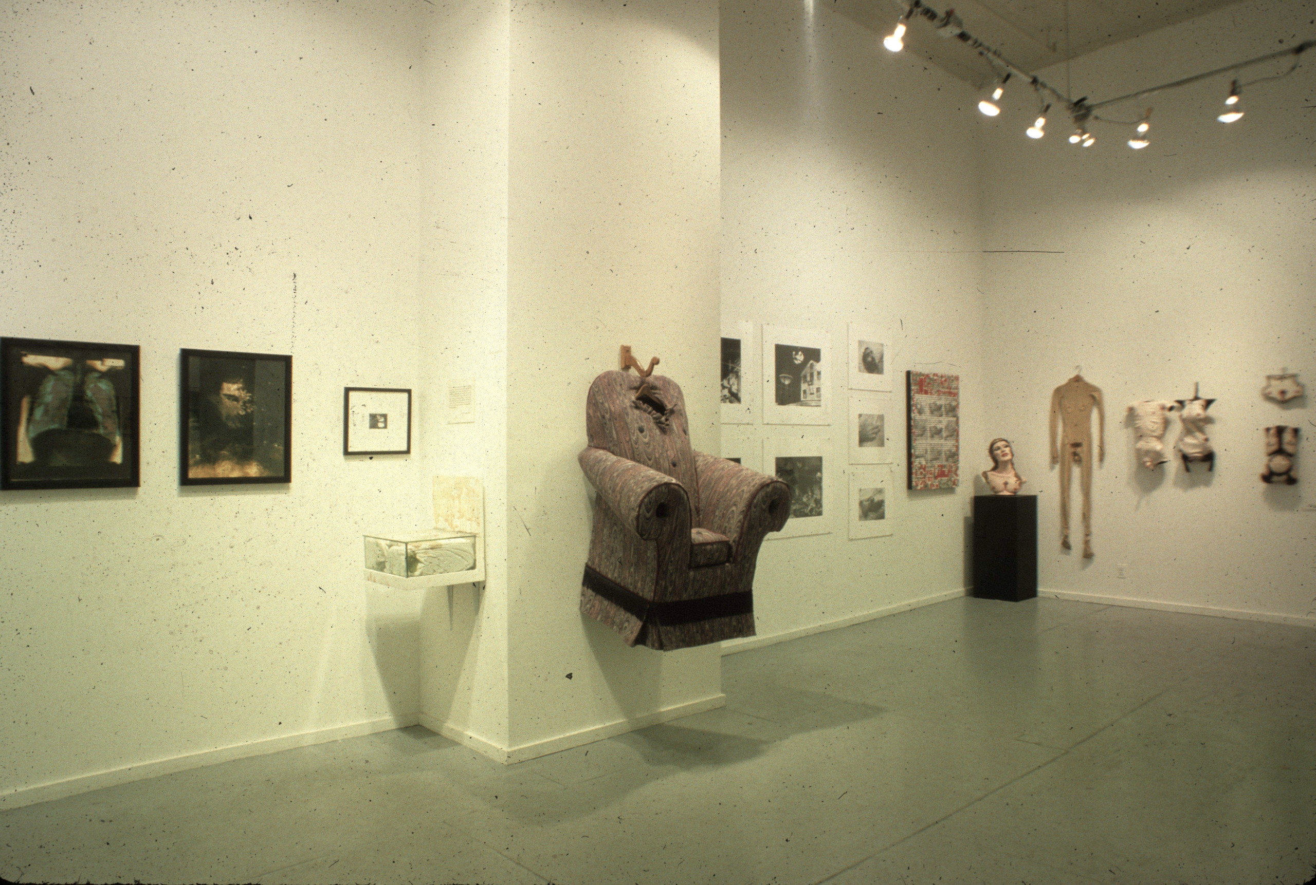 A wide view of a gallery featuring an array of paintings, sculptures, and photographs hung along a wall and wrapping around a corner.
