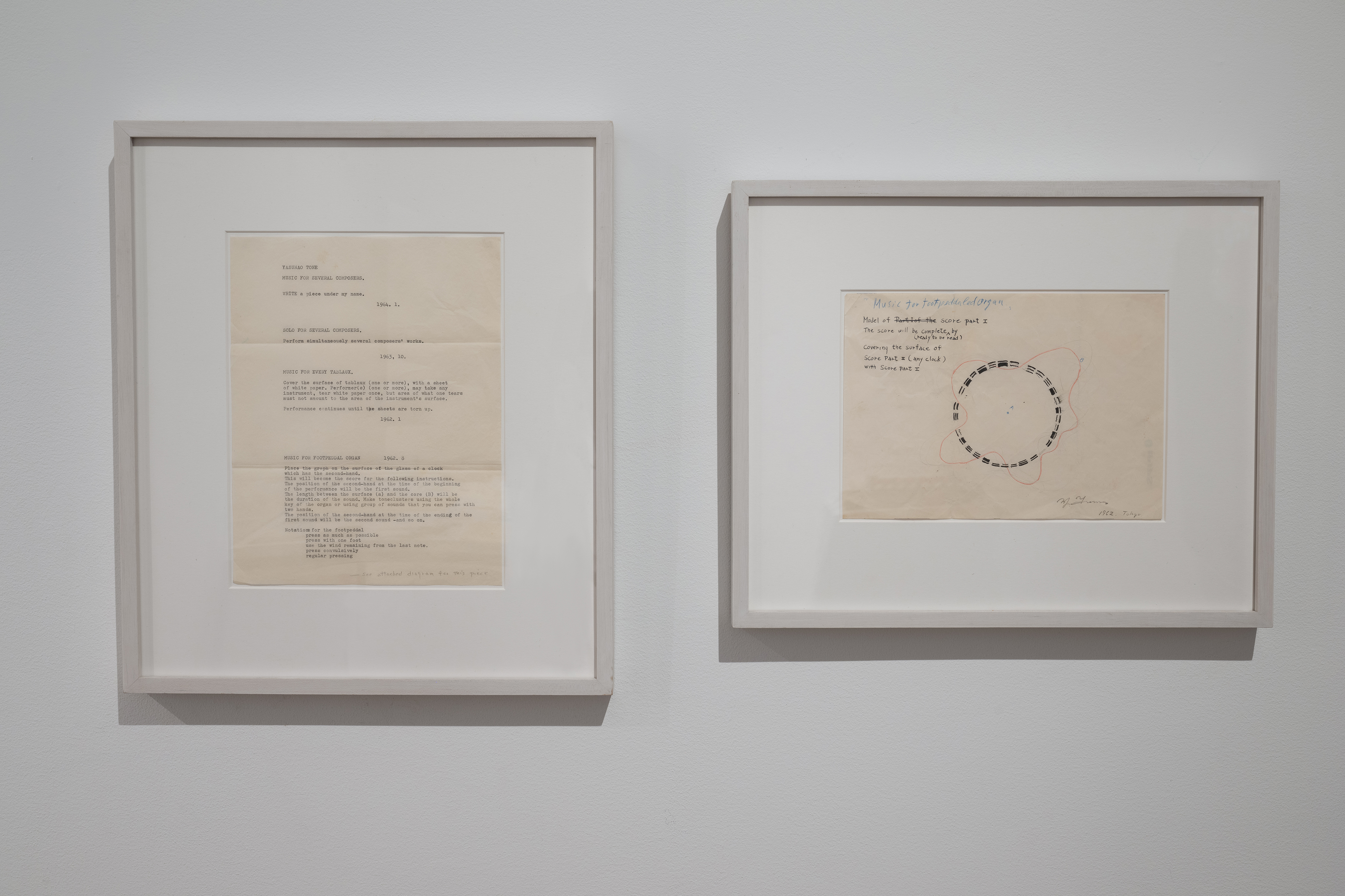 Color photograph of two framed works that are hung on the wall. The piece on the left contains typed instructions for a musical performance, and the piece on the left contains hand-written notes for another performance.